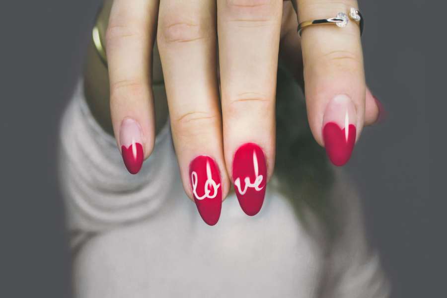 Nail art minimaliste rouge avec inscription "love" en blanc sur ongles ovales, main portant une bague.
