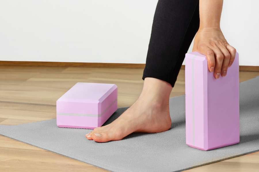 Une personne utilise des blocs comme accessoires de yoga sur un tapis gris pour stabiliser sa posture.