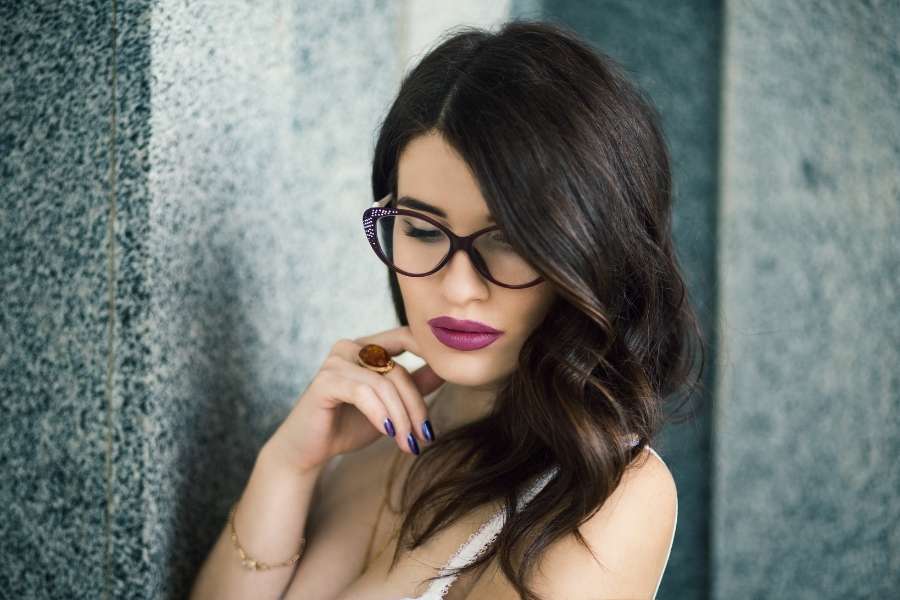 Un portrait élégant montrant un maquillage réussi avec des lunettes à monture épaisse et des lèvres fuchsia.